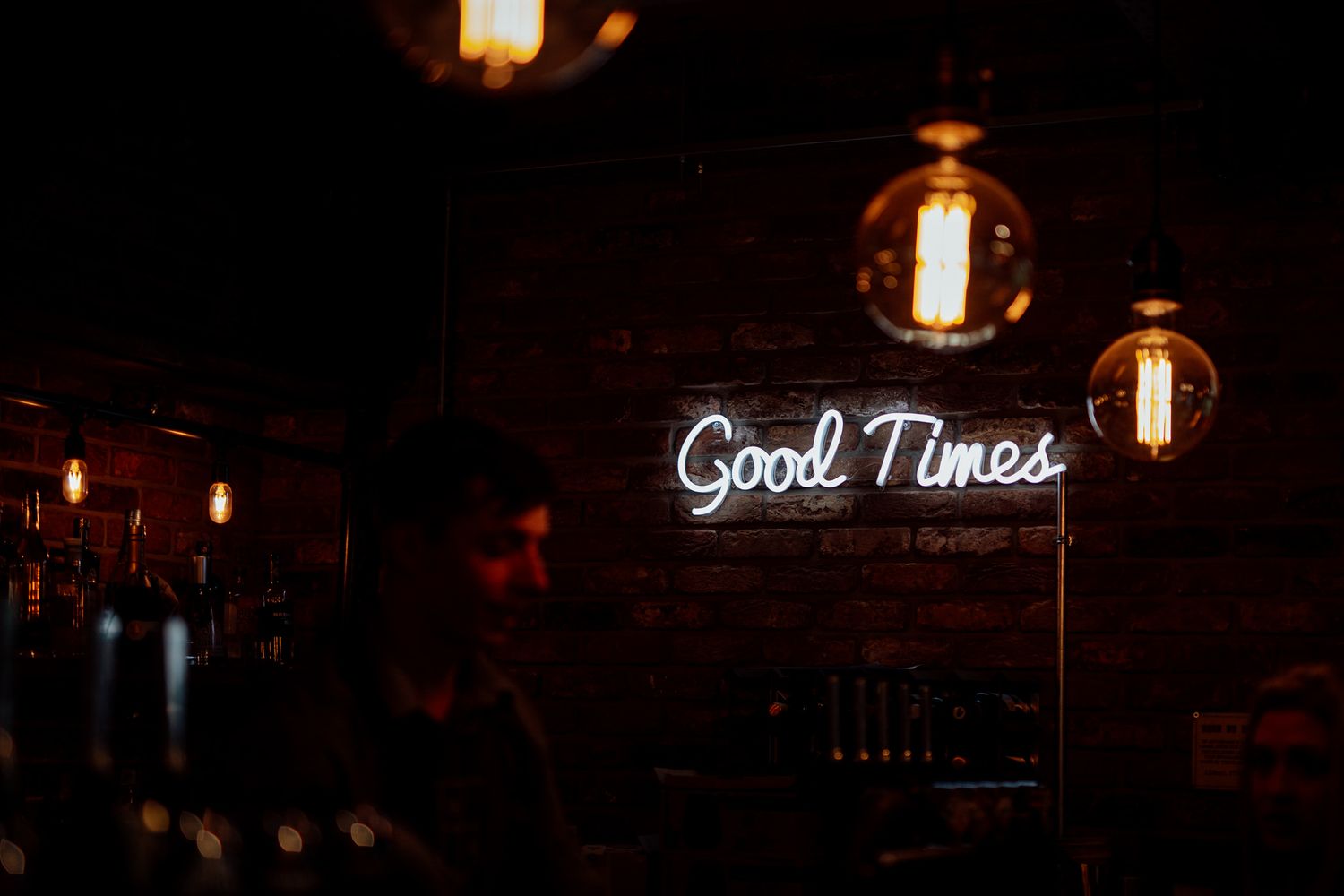 Neon 'Good Times' sign glowing against dark background with hanging pendant lights.