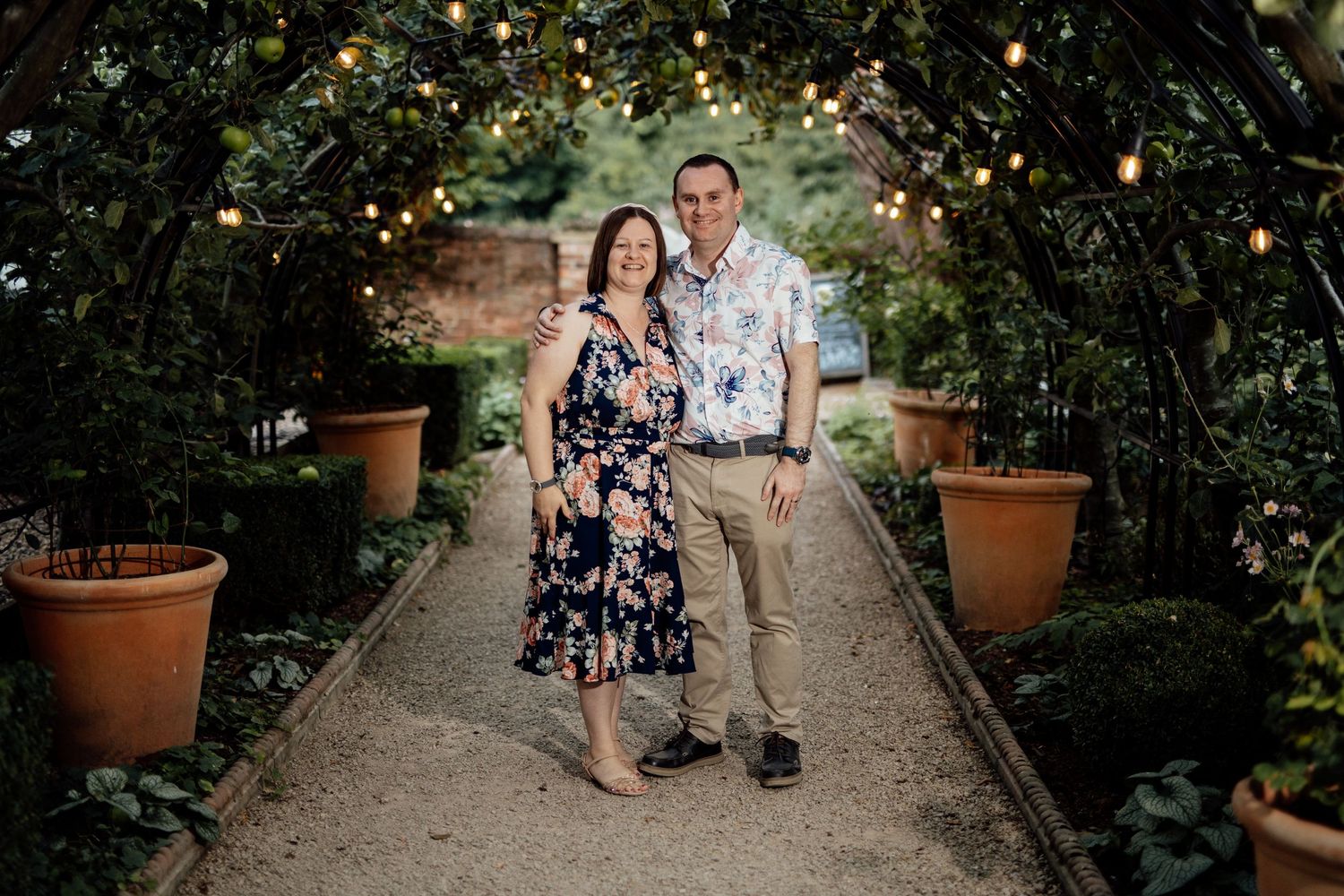 Garden pathway lined with potted plants and string lights creating romantic ambiance.