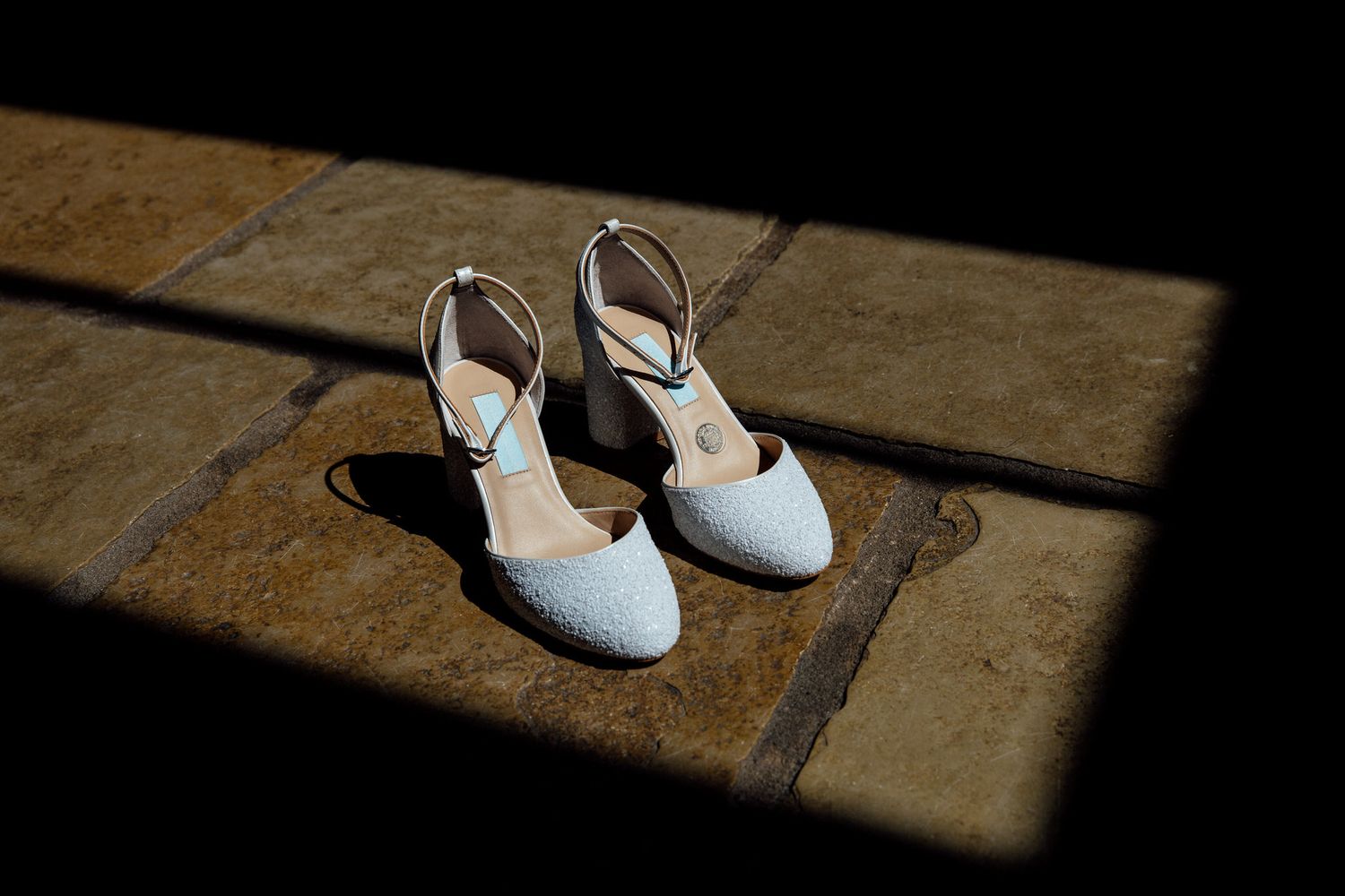 White bridal shoes casting dramatic shadows on stone floor.