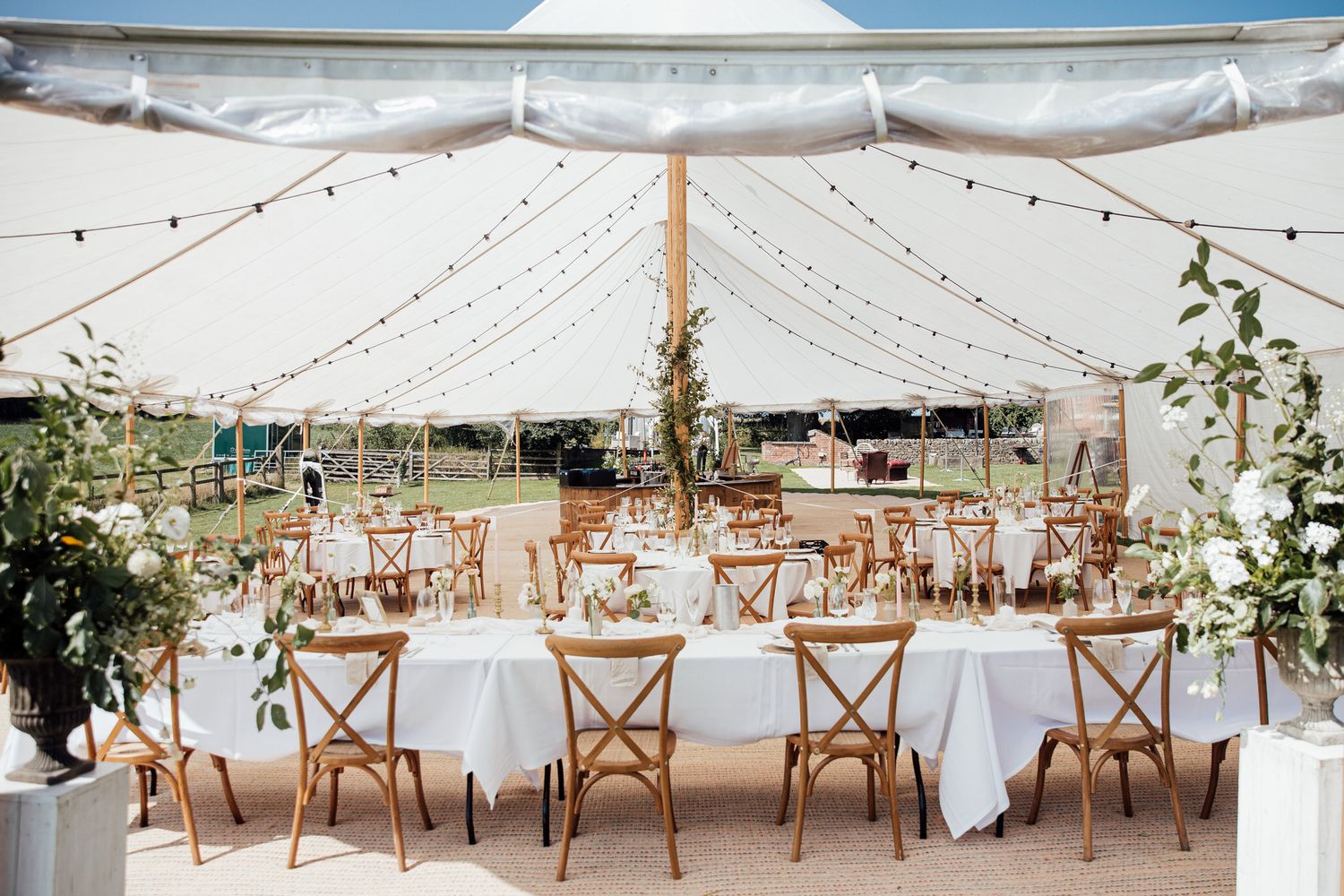 Elegant wedding reception setup with string lights and wooden chairs under white tent.