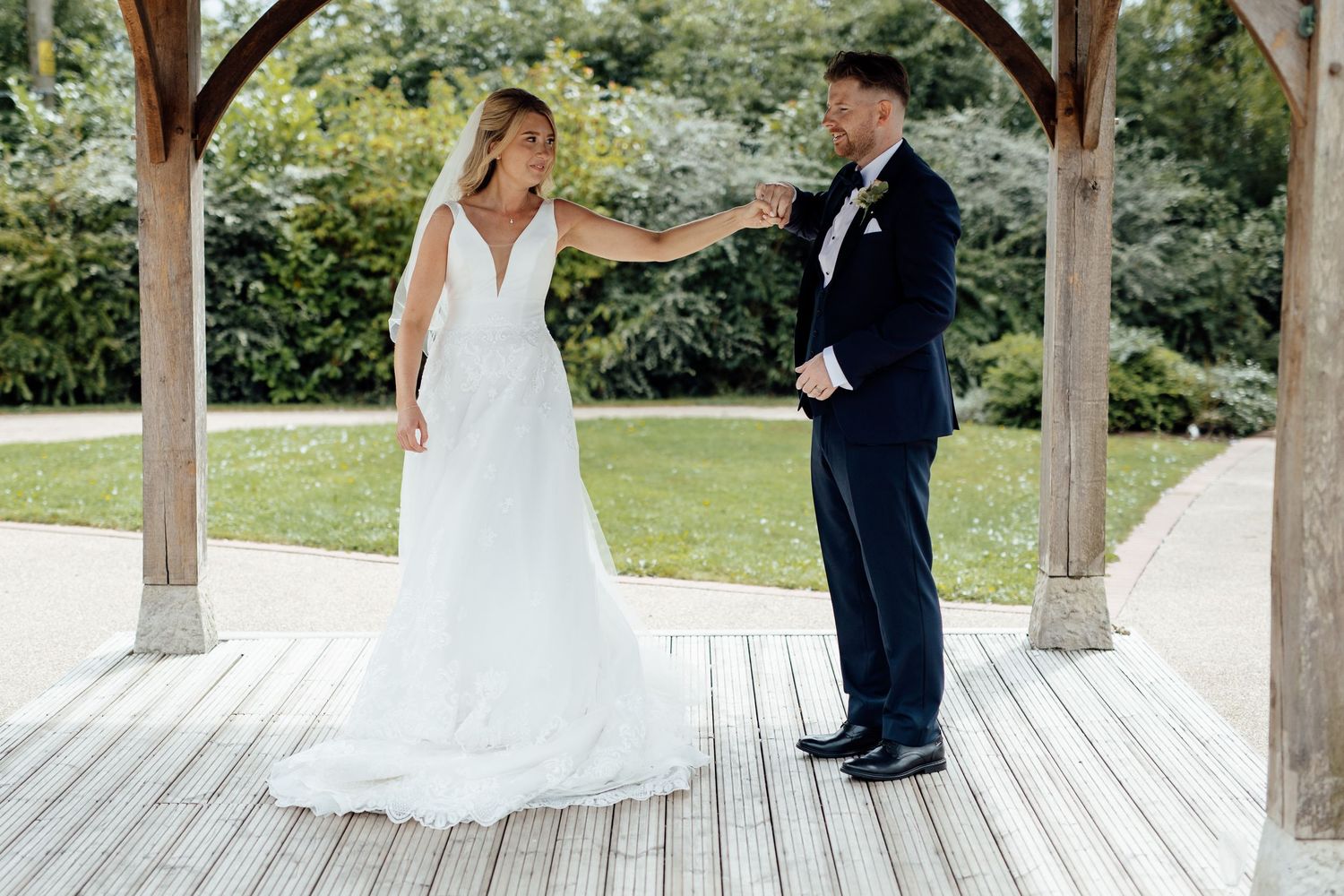 Wedding couple posing under wooden gazebo on outdoor deck.