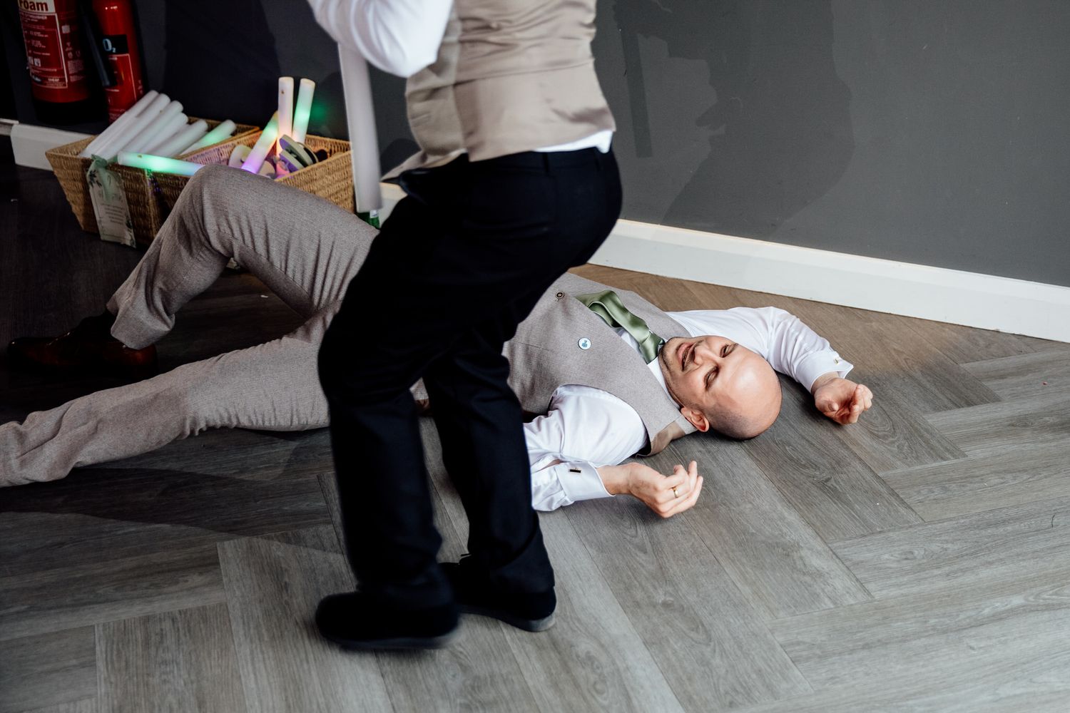 A playful moment during a wedding as a child lies on a gray hardwood floor.