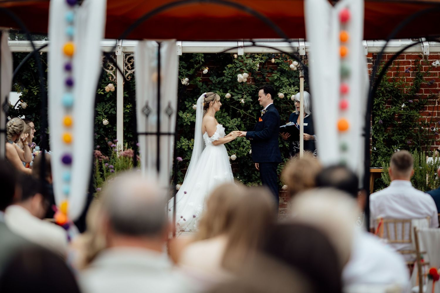 A wedding ceremony unfolds beneath a decorated gazebo as guests watch from their seats.