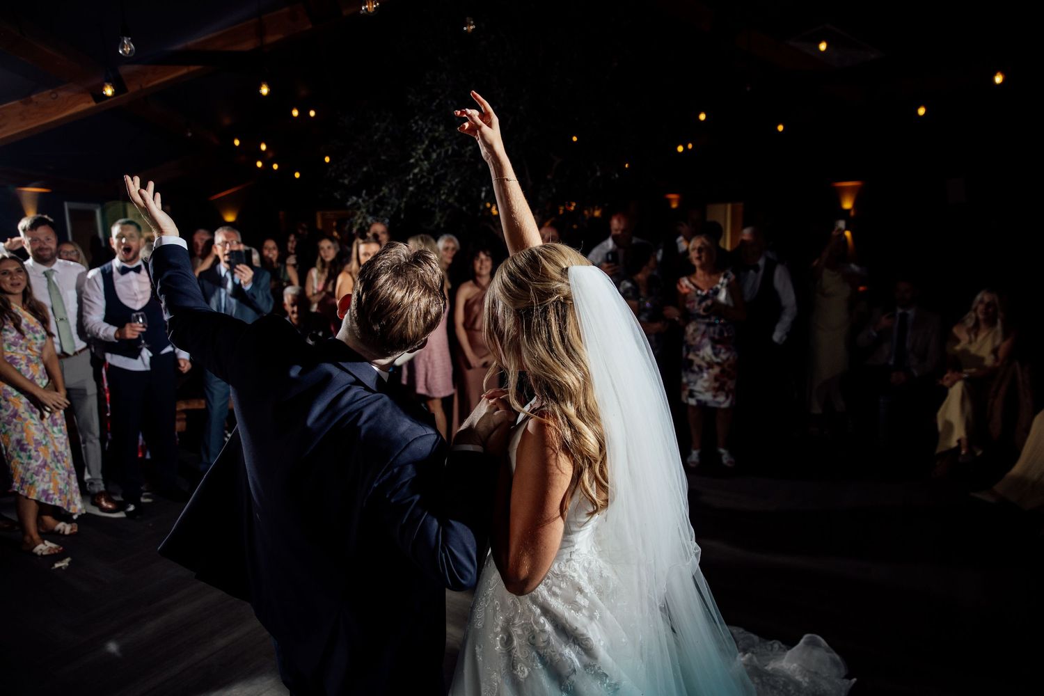 Wedding celebration on a dark dance floor with guests dancing.