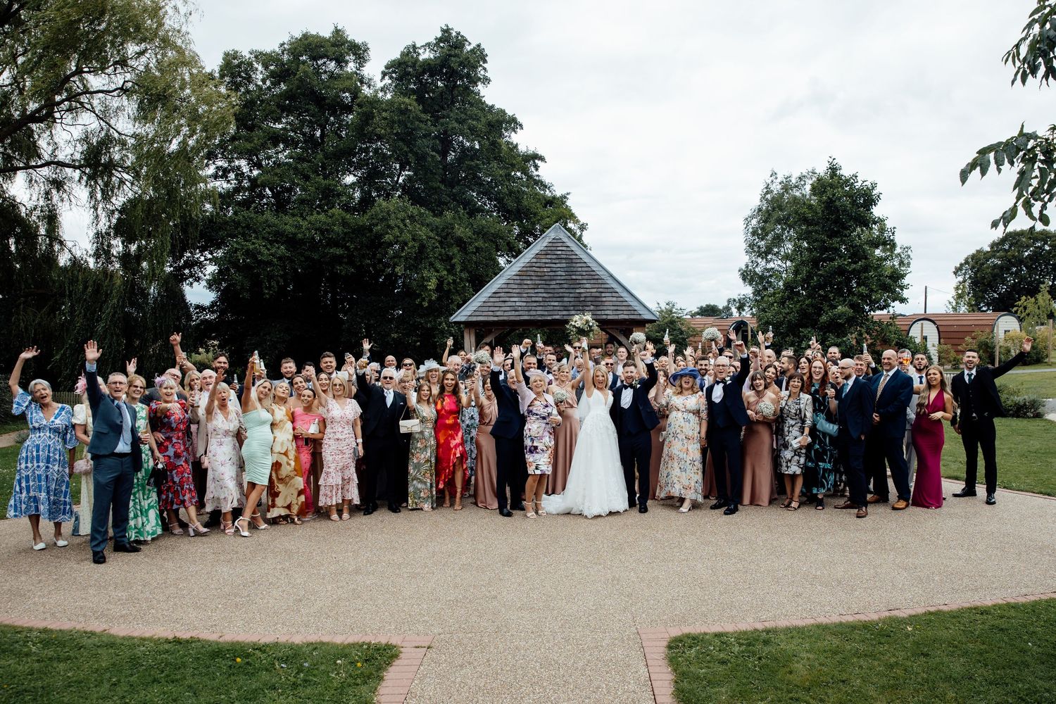 Large group of wedding guests pose together outdoors for formal photos.