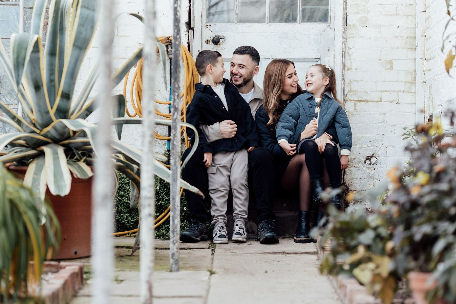 Modern family photoshoot against white brick wall with natural lighting.