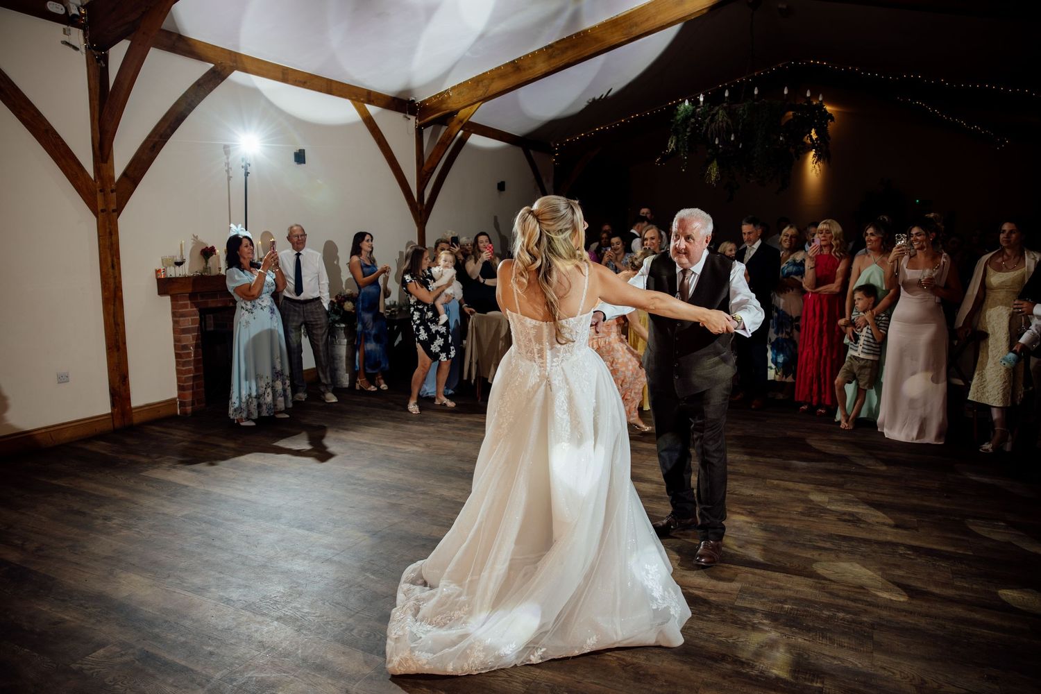 Bride dances with older gentleman on wooden dance floor at wedding reception.
