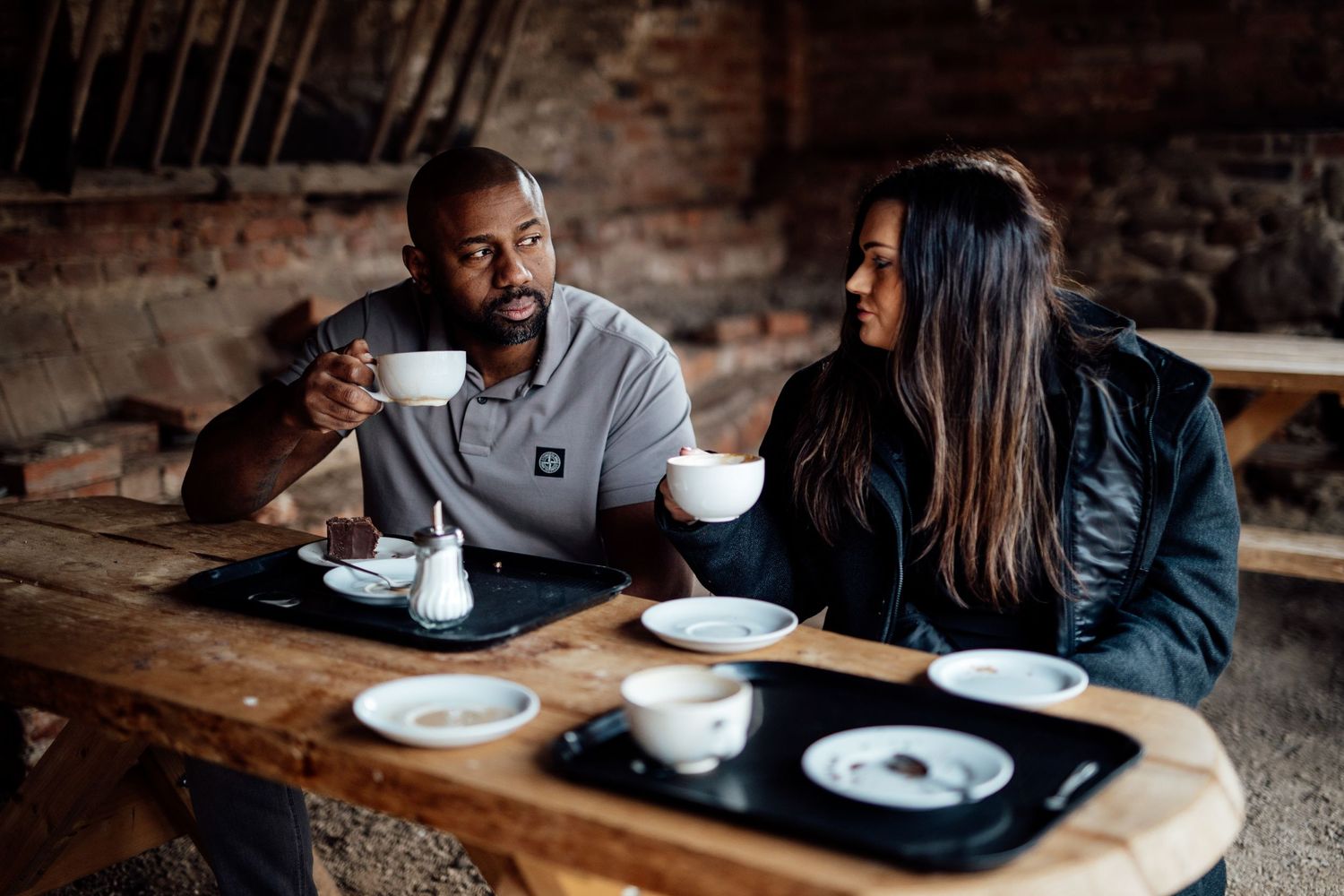 A couple shares an intimate moment while enjoying coffee and dessert at a rustic wooden table in a cafe.