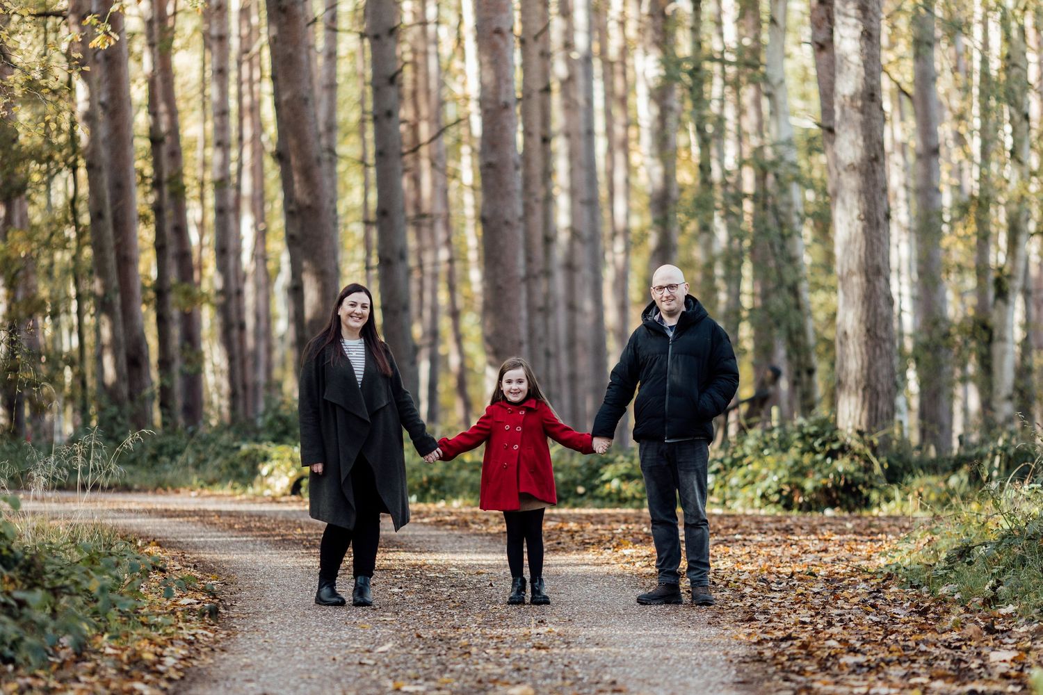 Family walking through tree-lined path in autumn forest.