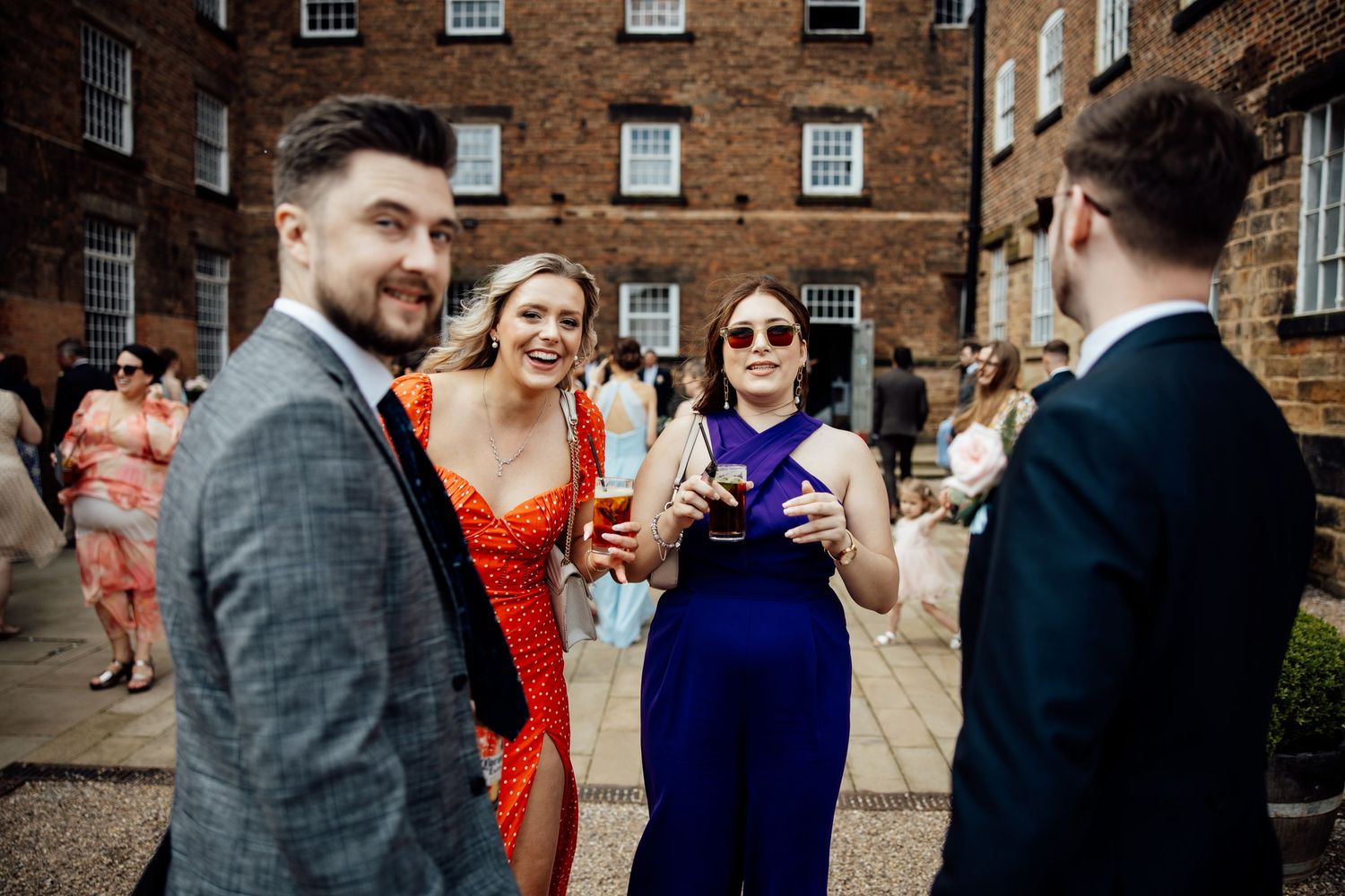 Wedding guests in formal attire gathered outside a brick building during a celebration.