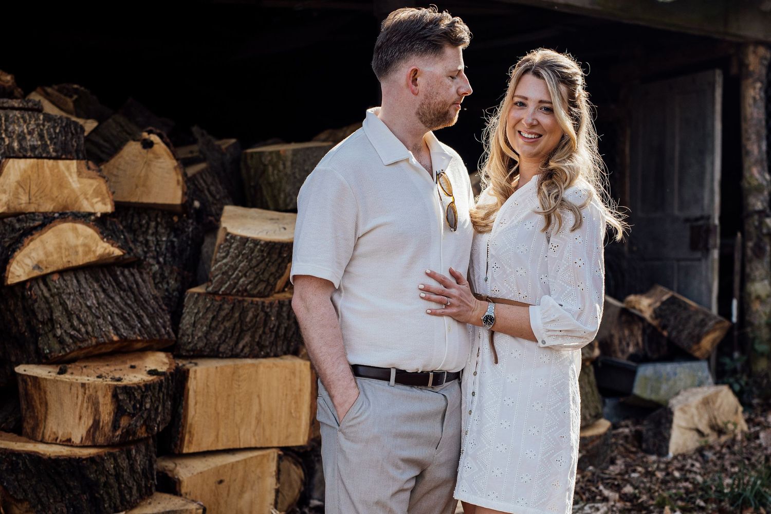 A couple shares tender moments near rustic stacked firewood during their engagement shoot.