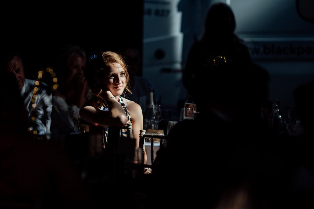 Dramatic lighting captures emotional reactions during wedding reception speeches.