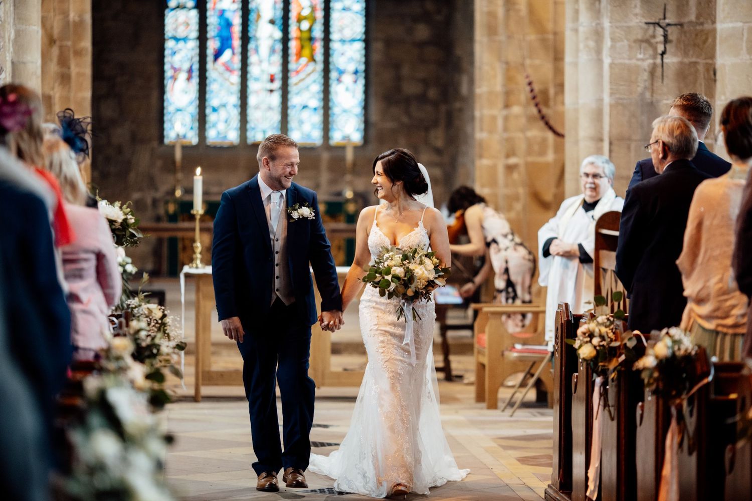 A wedding ceremony taking place inside a traditional stone church with beautiful stained glass windows.