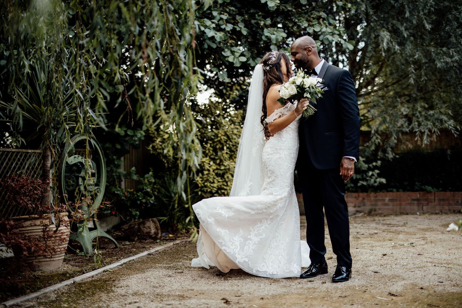 A romantic wedding portrait in a lush garden setting with elegant attire and natural greenery.