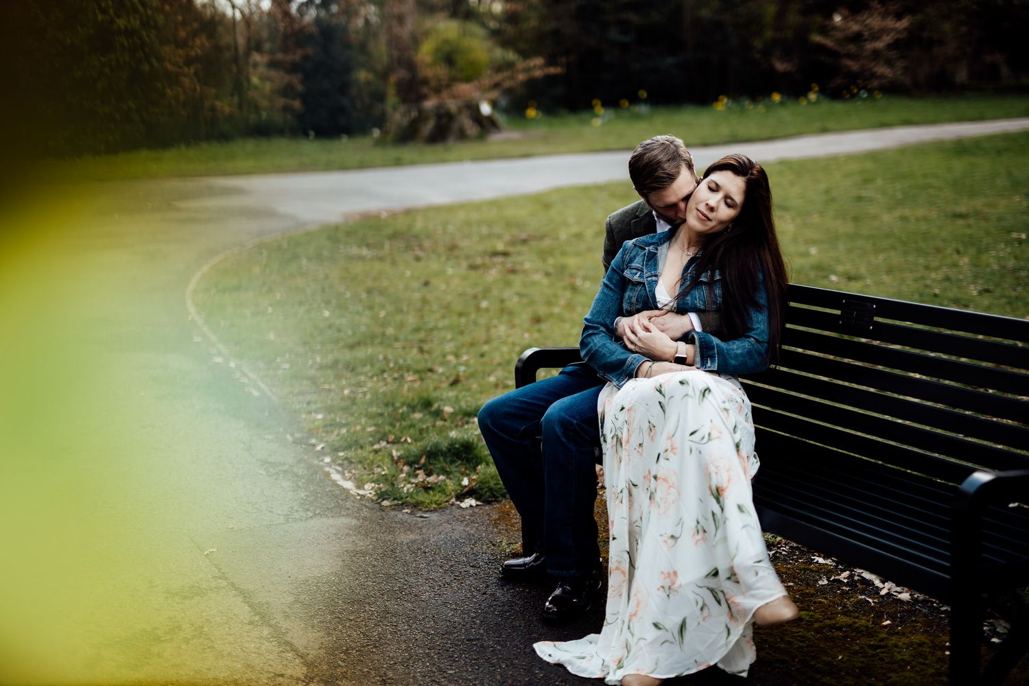 A couple shares an intimate moment while sitting on a park bench surrounded by nature.