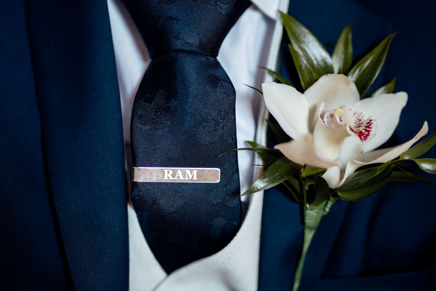 Close-up of white orchid boutonnieres pinned to navy blue suits.