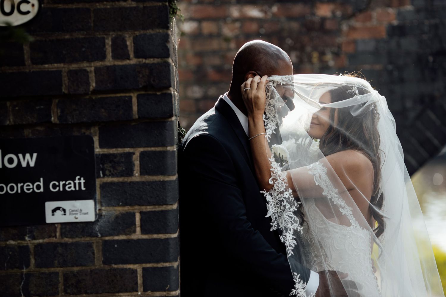 Wedding couple walking near brick wall with soft lighting.