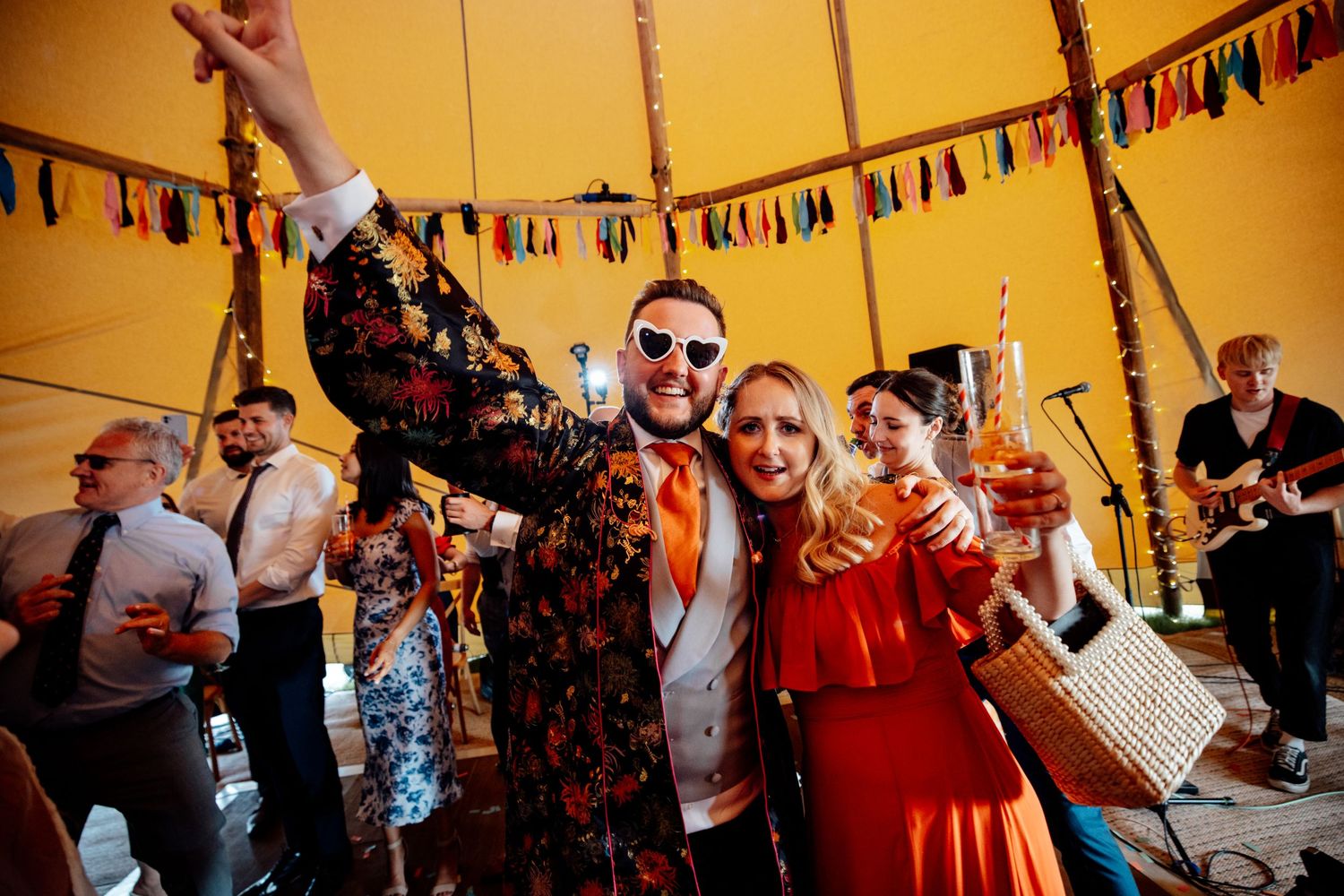 Festive celebration under a tent with colorful bunting decorations and live band performing.