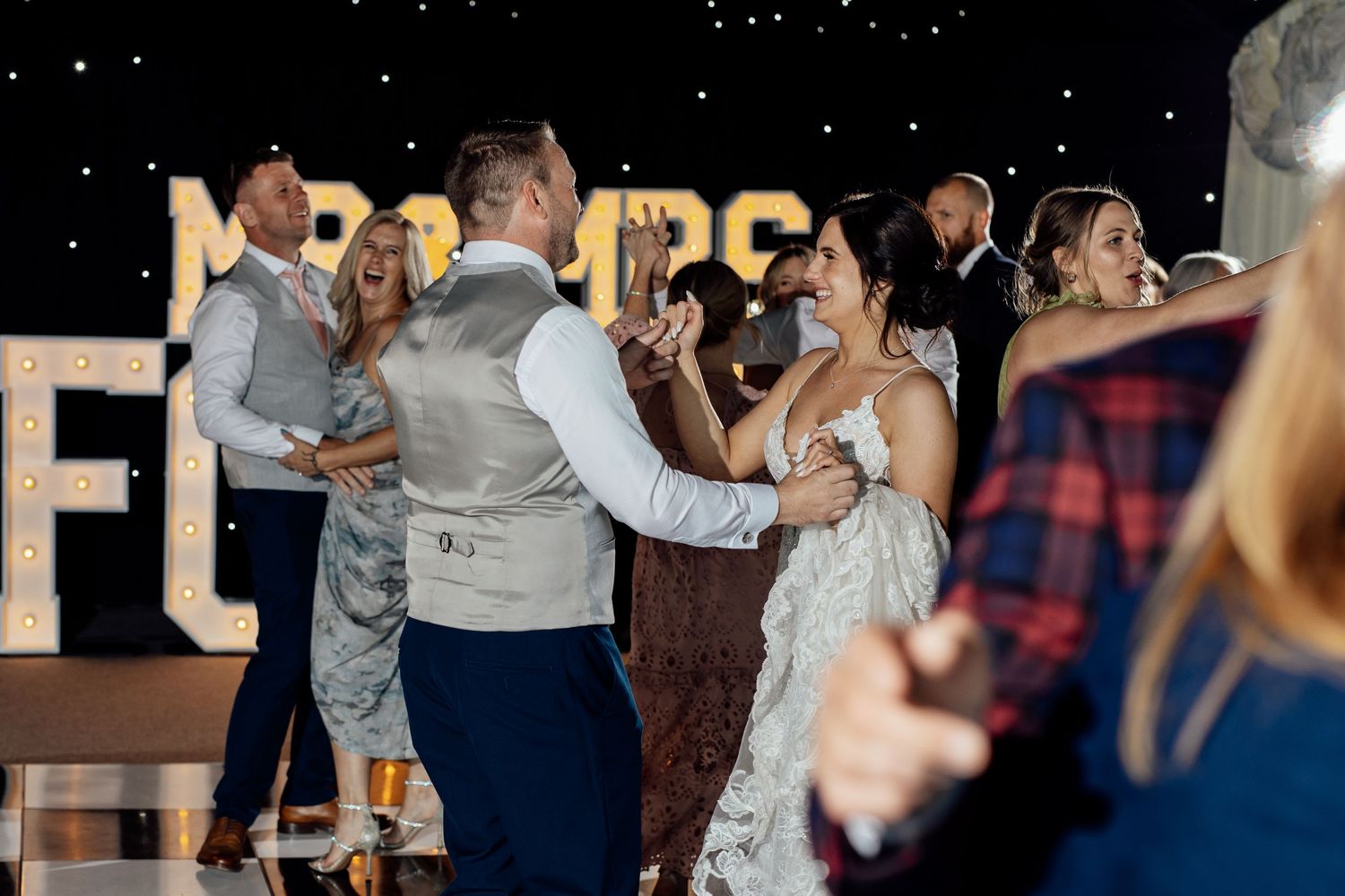Wedding reception dance floor with illuminated letters and guests dancing.