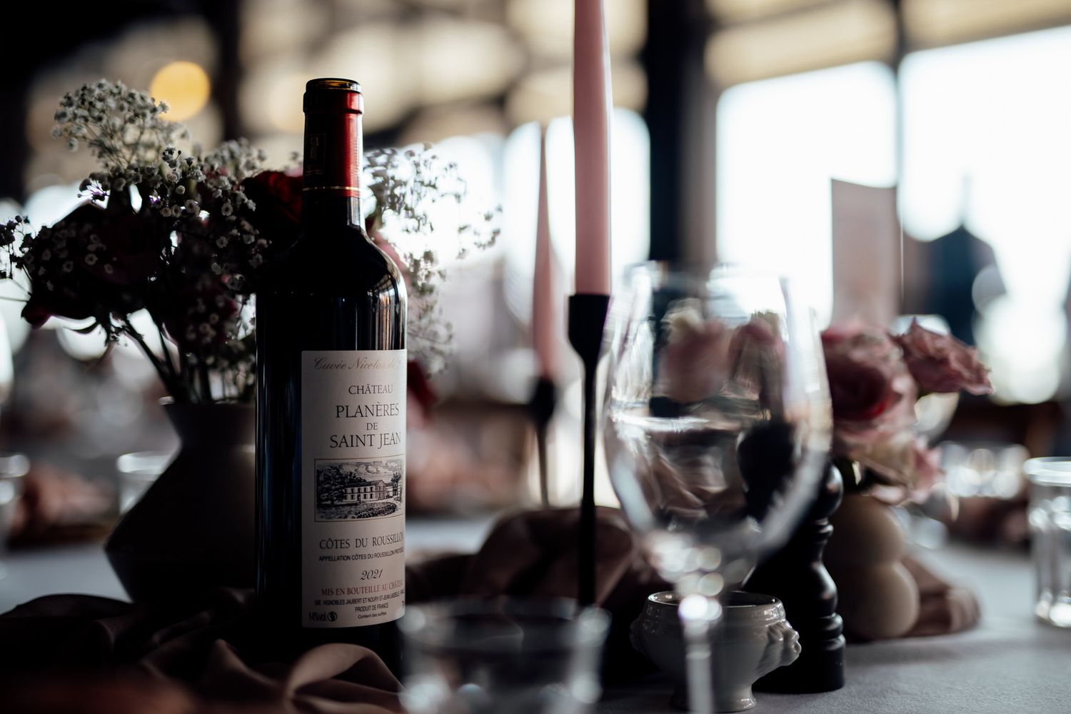 Wedding reception table details with wine bottles and soft focus floral arrangements.