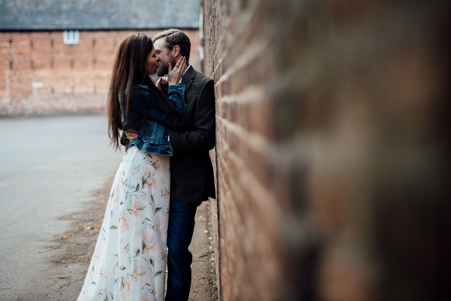 Couple shares intimate moment against rustic brick wall background.