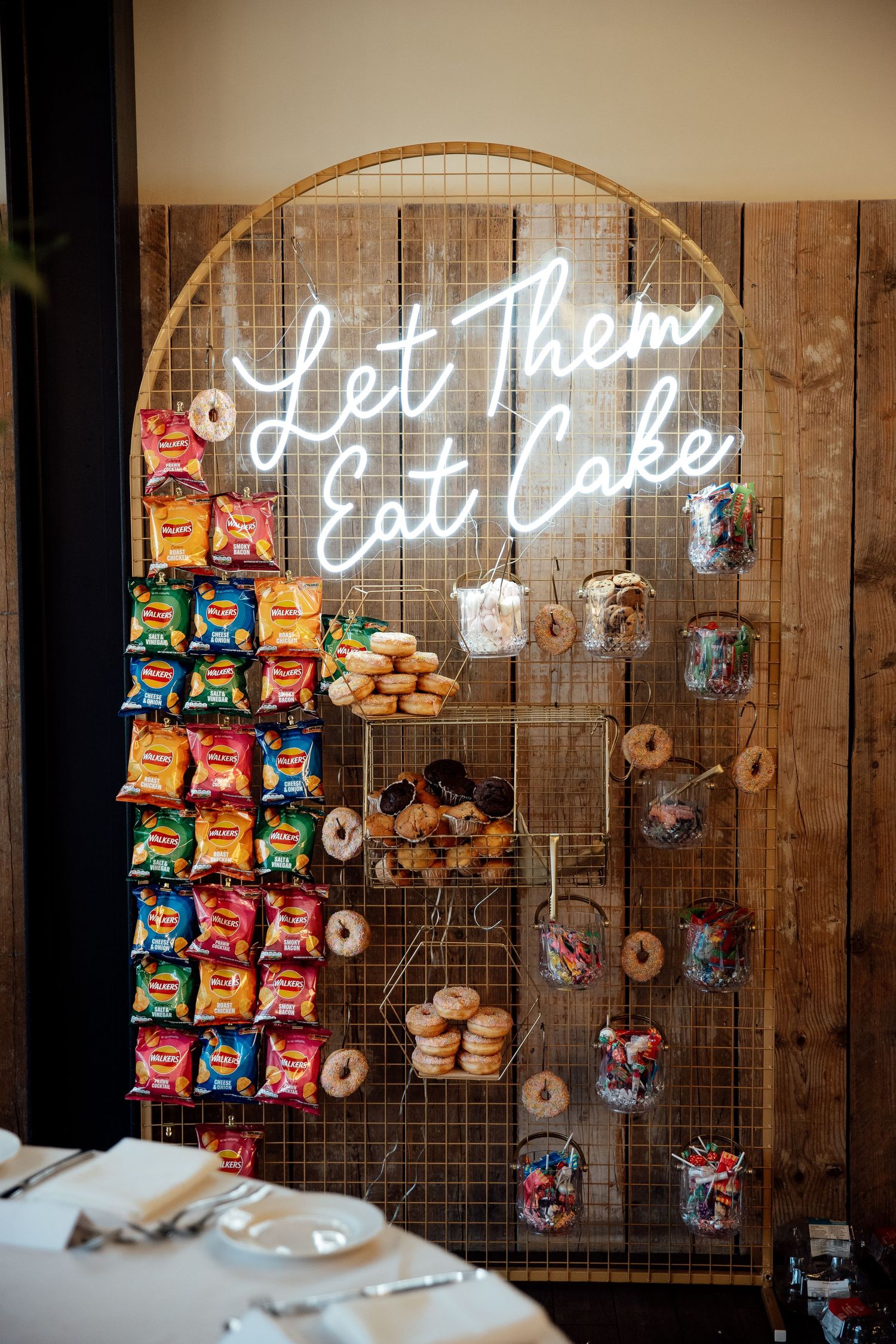 Rustic wooden wall with neon 'Let them eat cake' sign and snack display.
