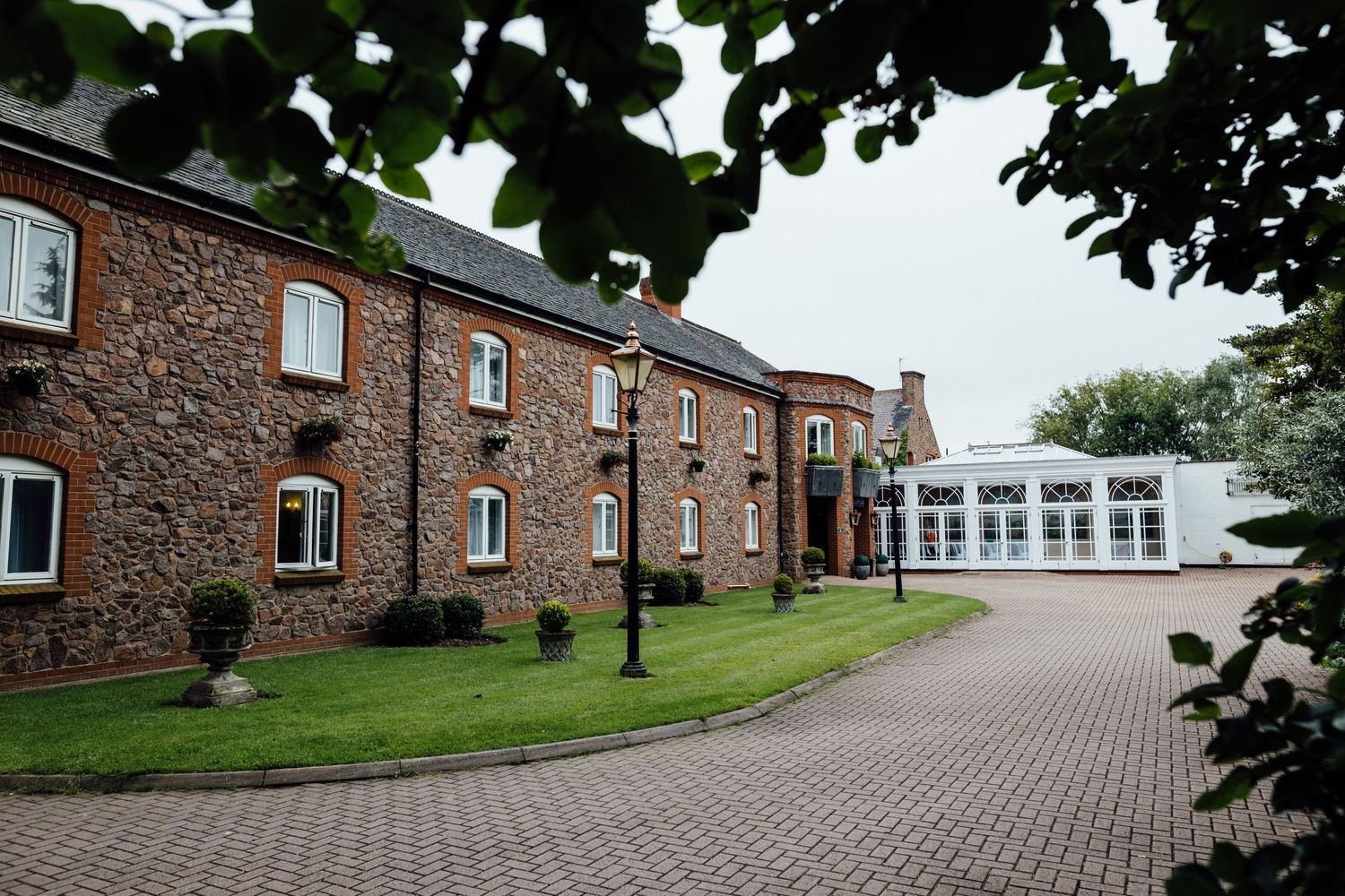 Exterior view of brick buildings with cobblestone driveway and landscaped grounds.