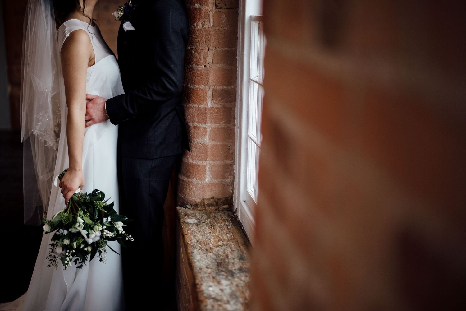 Intimate moment captured against exposed brick wall at wedding venue.