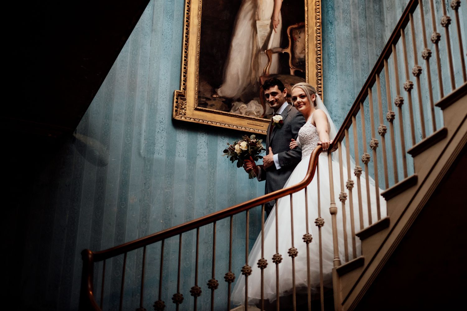 Wedding party descending a grand curved staircase in an elegant historic interior.