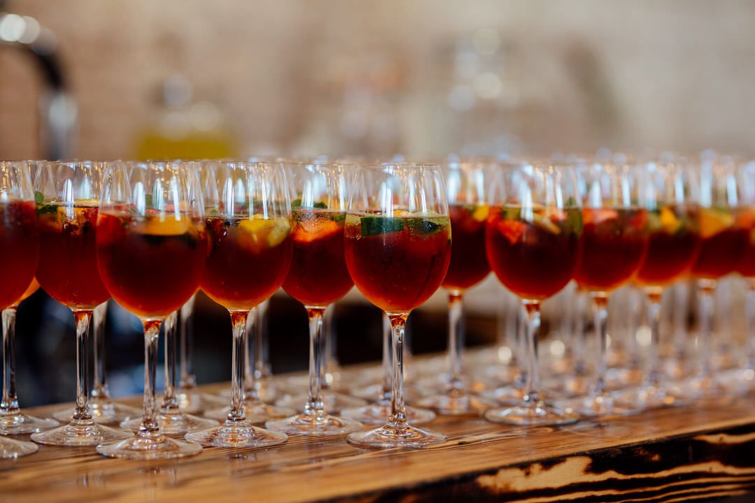 Long row of red cocktails in wine glasses arranged on a bar for wedding reception.