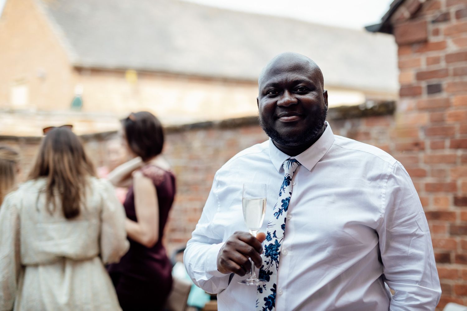 Wedding party members interacting outdoors against a brick wall backdrop.