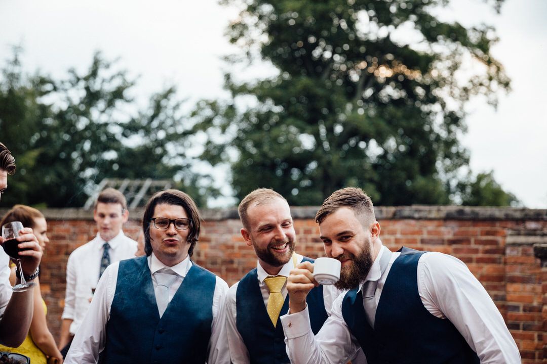 Wedding guests gather outdoors near a brick wall during a celebration.