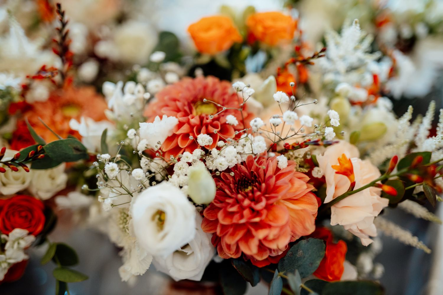 Colorful wedding floral arrangement with coral dahlias, white roses and mixed seasonal blooms.