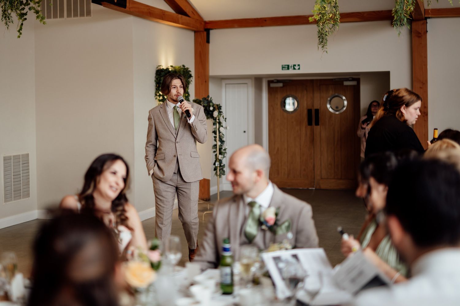 Wedding guests seated at tables during a reception in a rustic wooden beam venue.