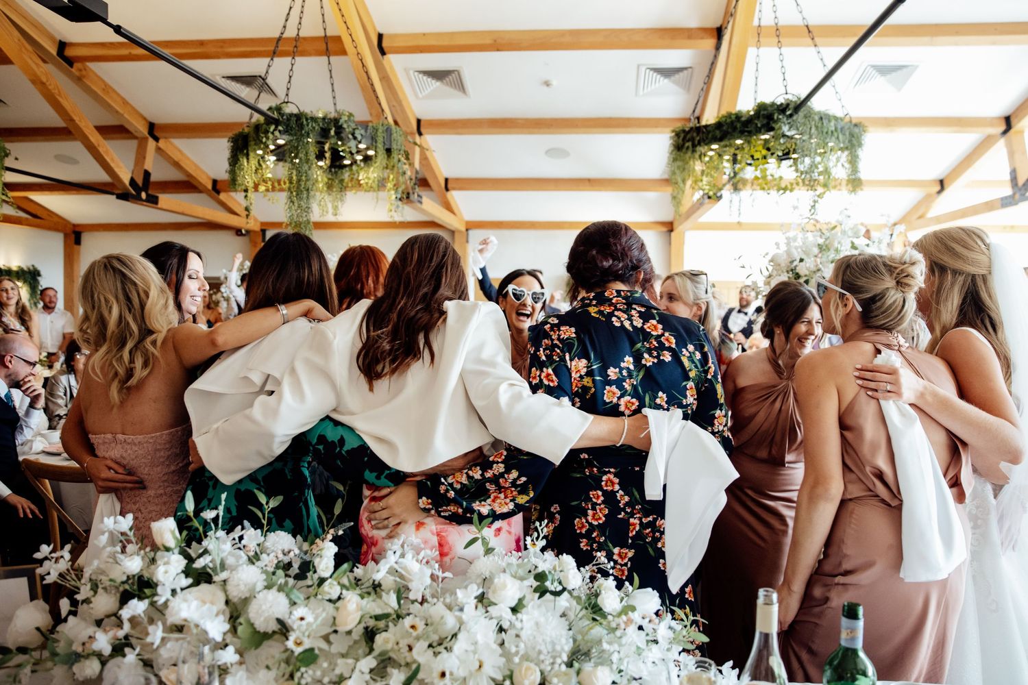 Wedding reception celebration with guests dancing under rustic wooden beams decorated with greenery.