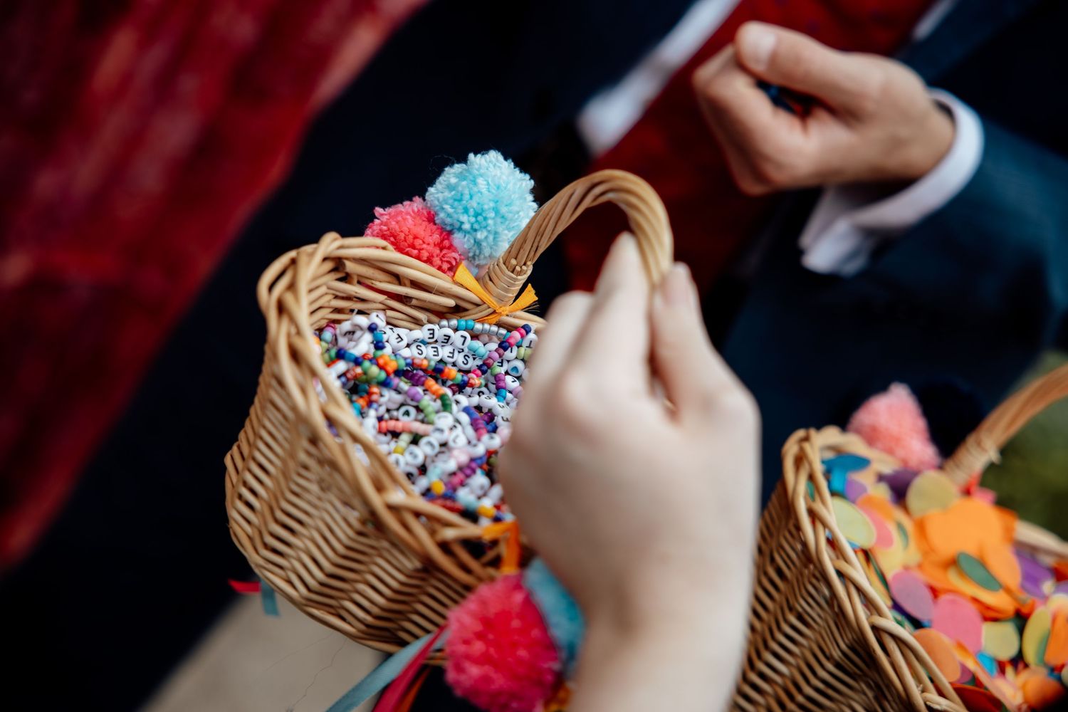 Close-up of hands reaching into wicker basket filled with colorful confetti and pom-poms.
