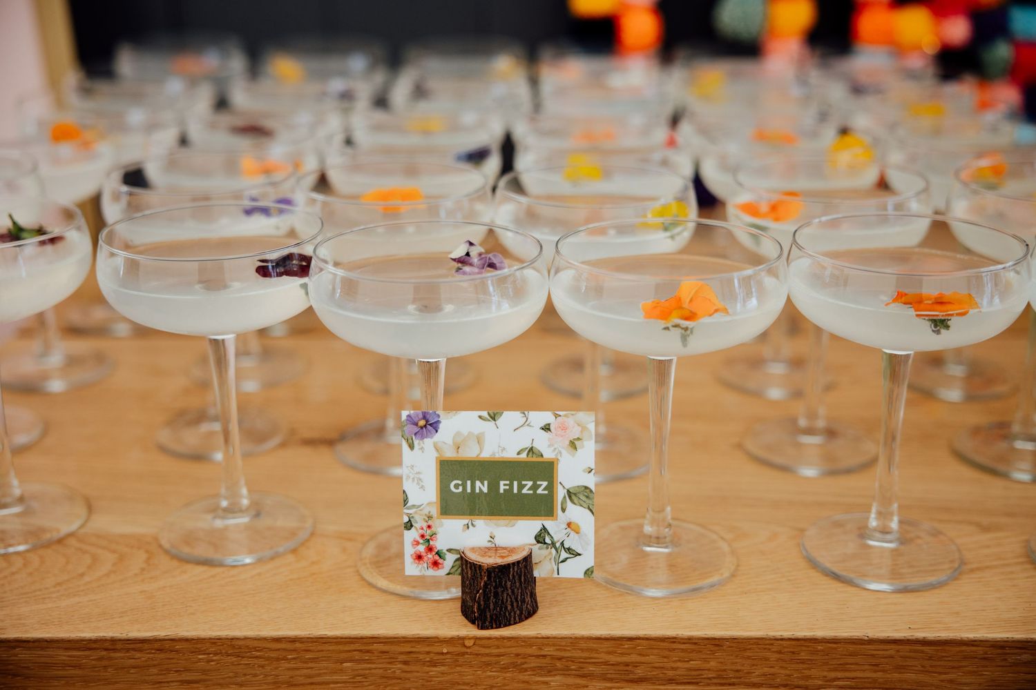 Row of wine glasses with orange flower petals on wooden table at reception.