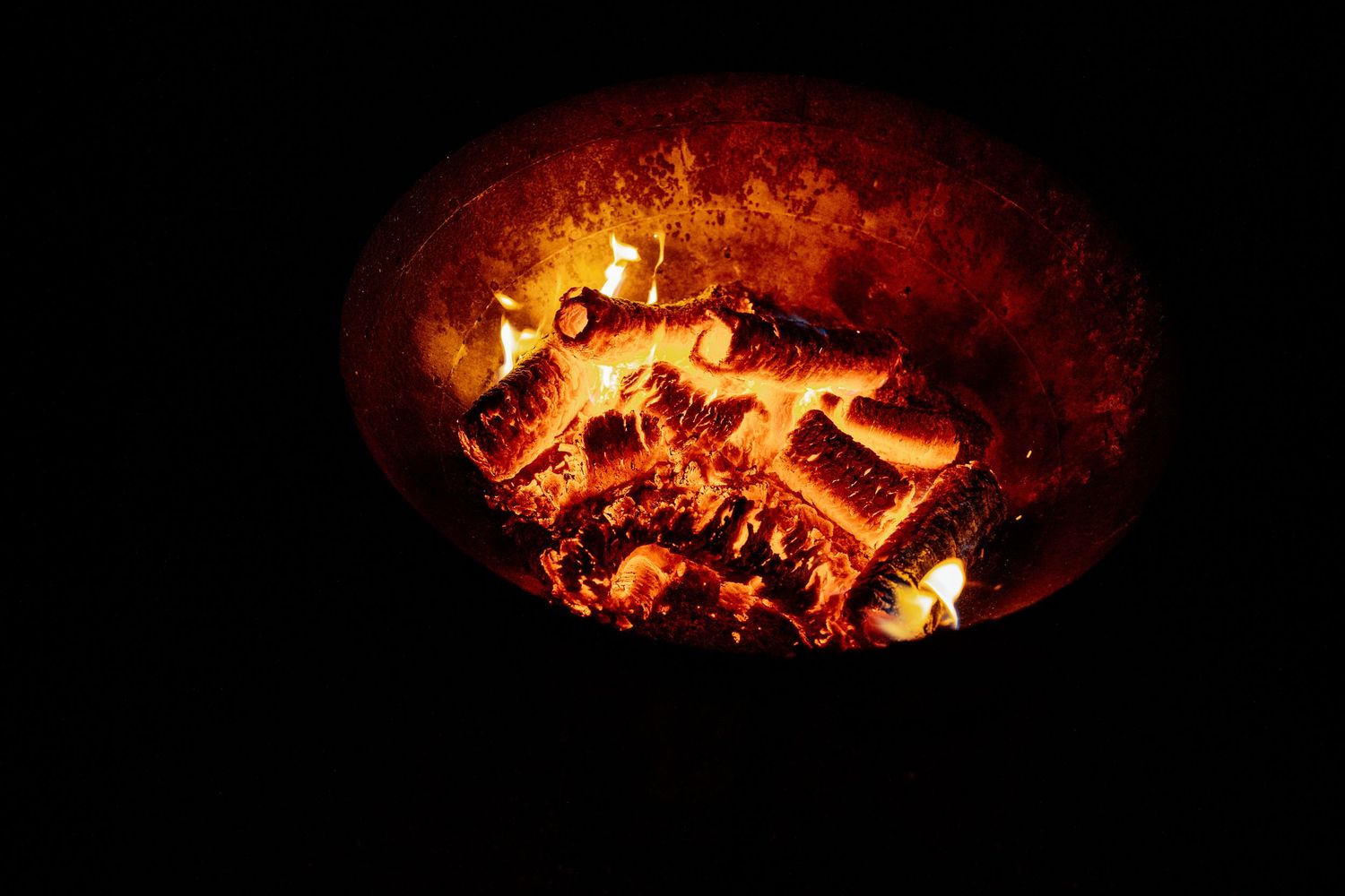 Glowing hot embers and burning logs in a fire pit create a warm orange ambiance.
