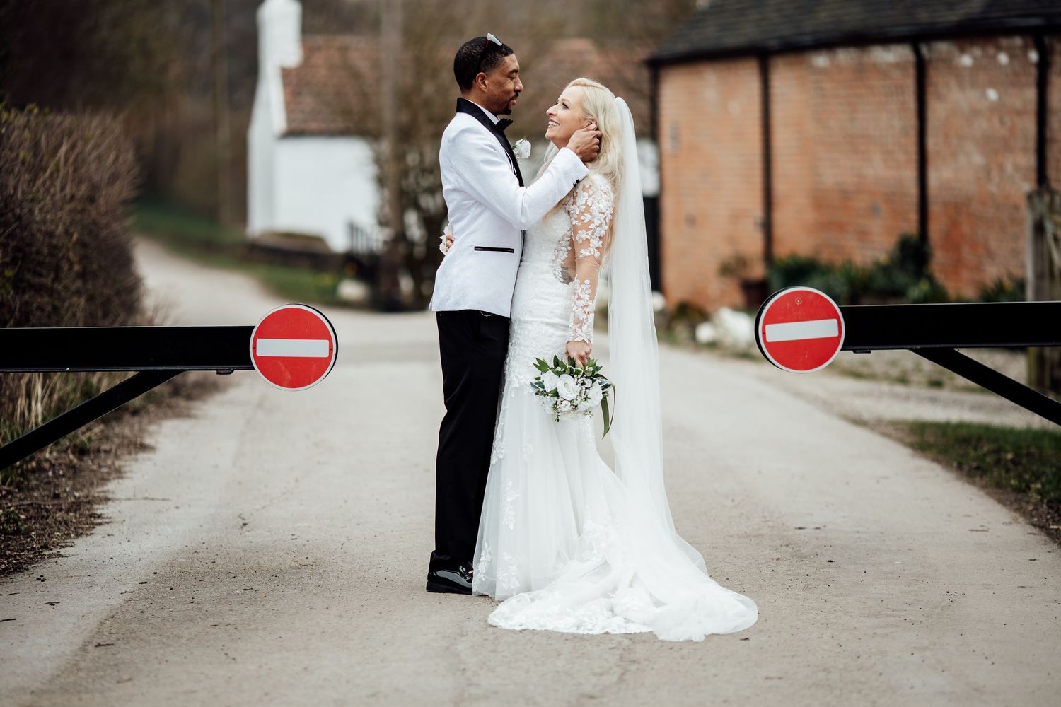 Interracial wedding couple share tender moment on rural road flanked by no entry signs in countryside.
