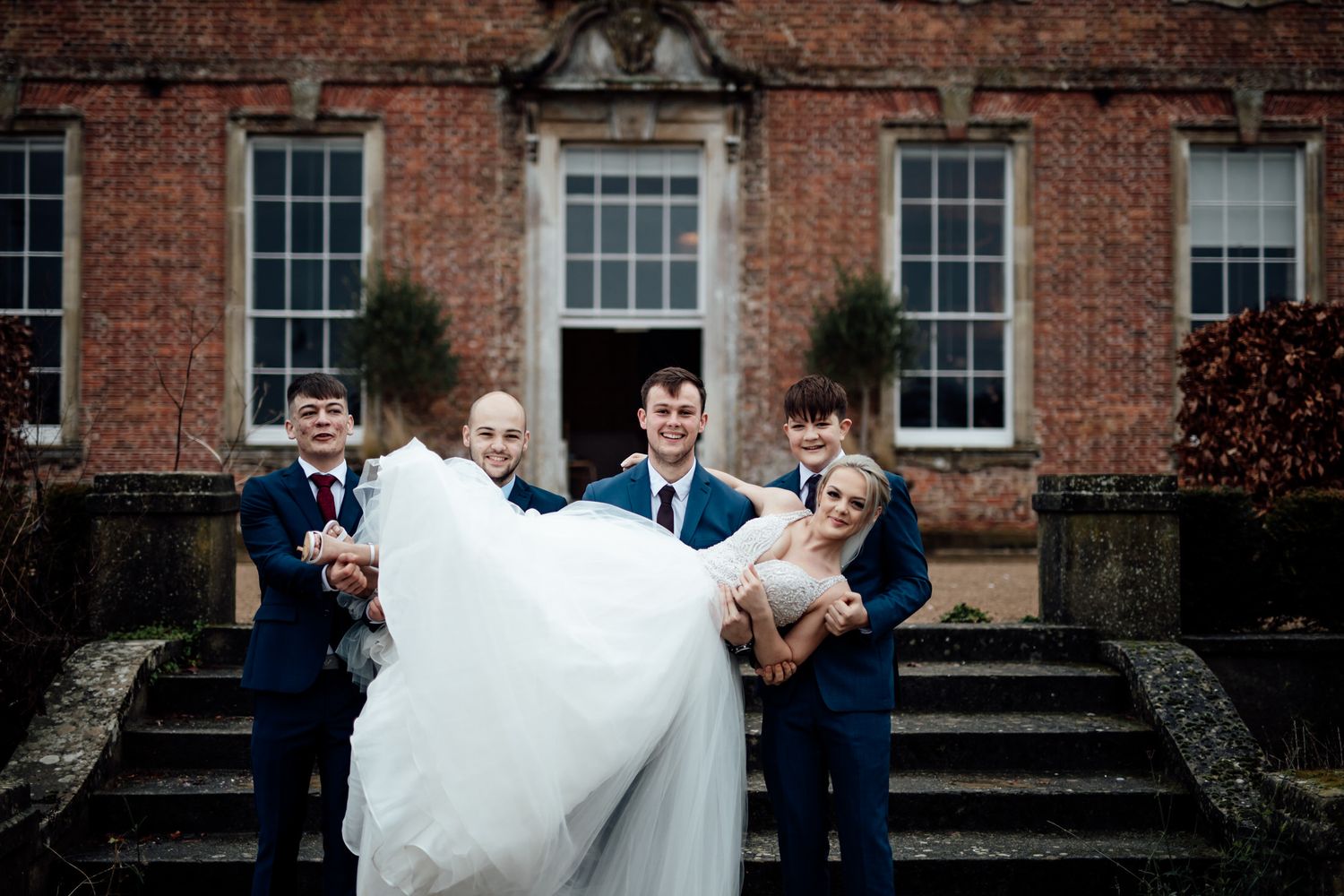 Wedding party poses outside a grand red brick Georgian-style building.