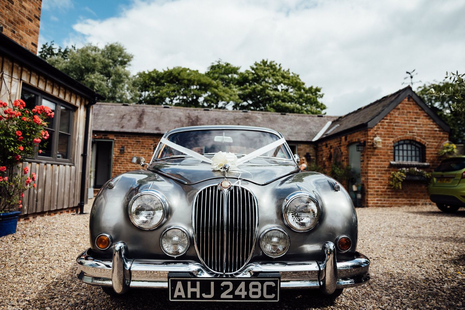 Vintage silver classic cars displayed in front of rustic brick buildings.