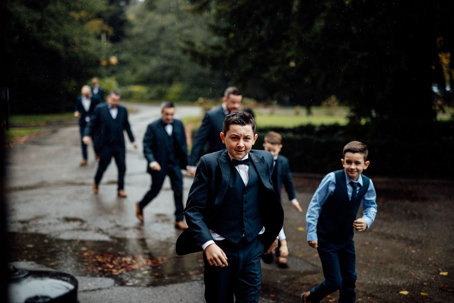 Wedding party walking along a rainy path in navy blue suits.