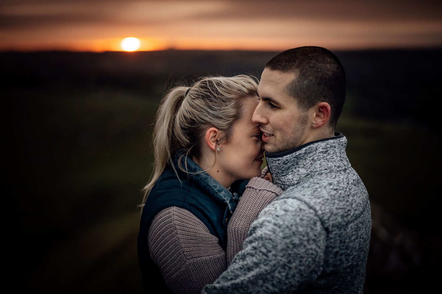 A couple shares an intimate moment against a dramatic sunset sky.