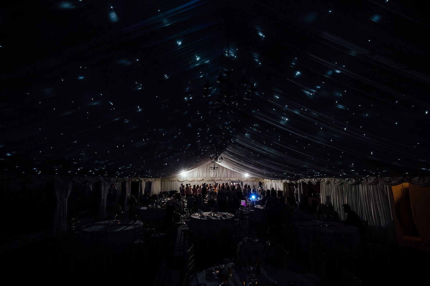 Large wedding reception tent illuminated at night with dramatic lighting effects.