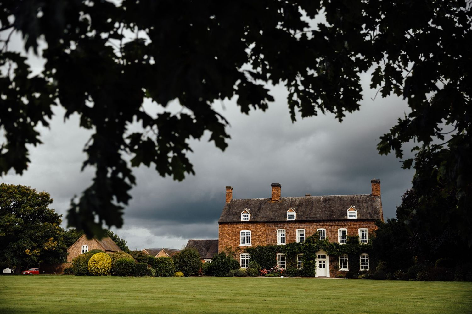 Dramatic view of a grand brick manor house with stormy clouds overhead.