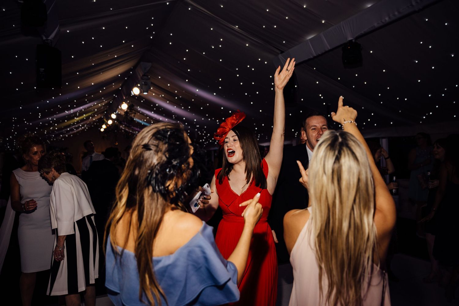 Wedding reception dance floor filled with guests celebrating under starlit ceiling.