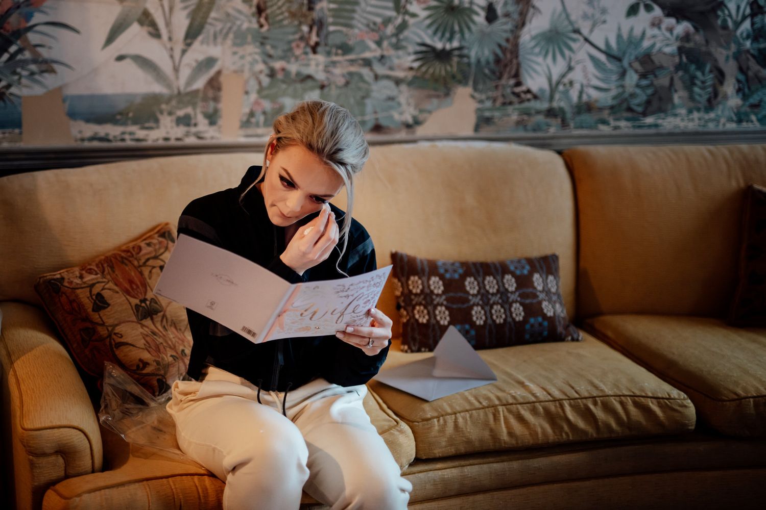Person reading document while sitting on beige couch with patterned wallpaper background.