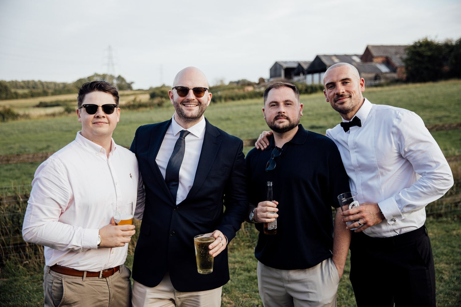 Groomsmen enjoying drinks and laughing together at outdoor wedding reception.