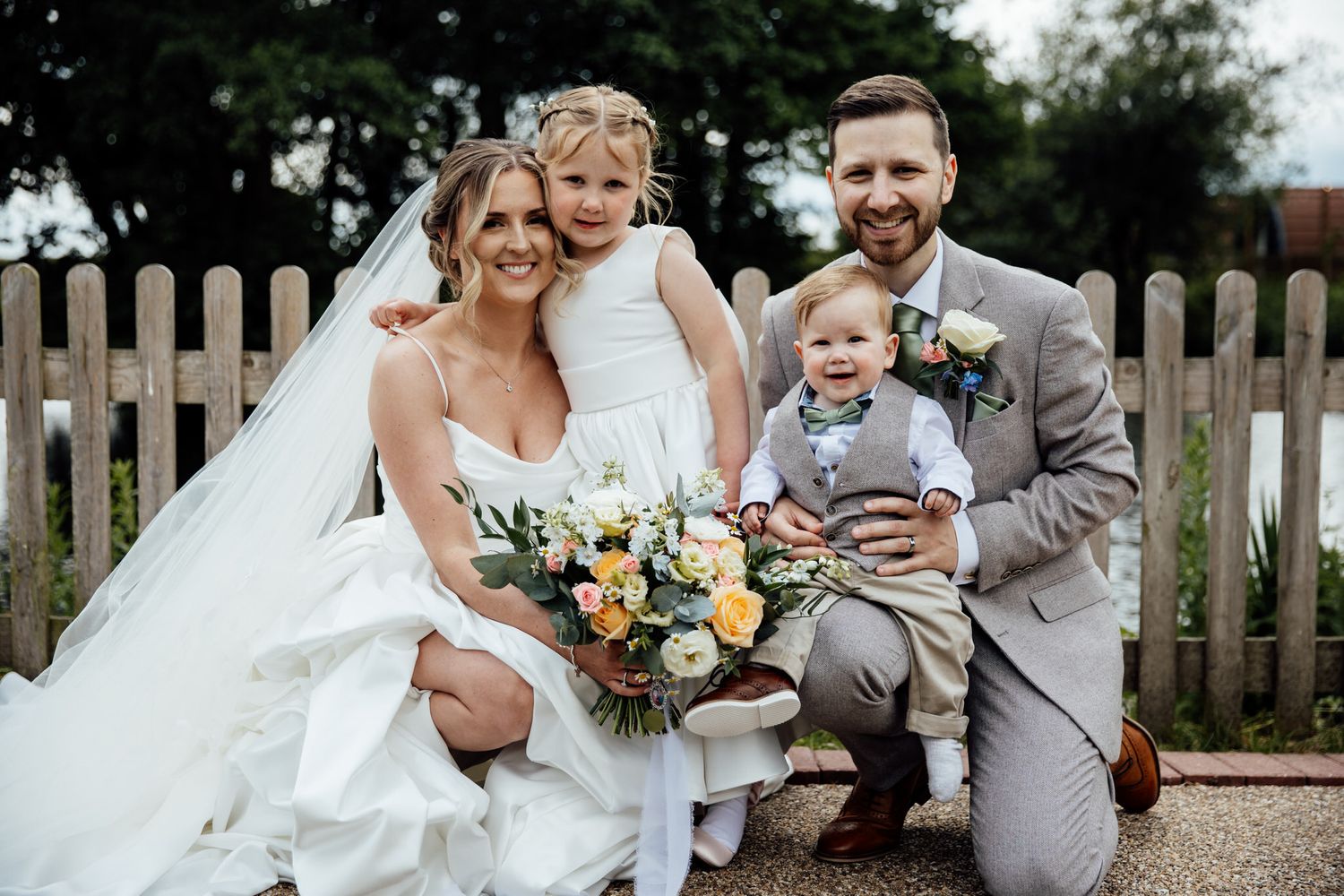 Wedding party posing together outdoors near a wooden fence.