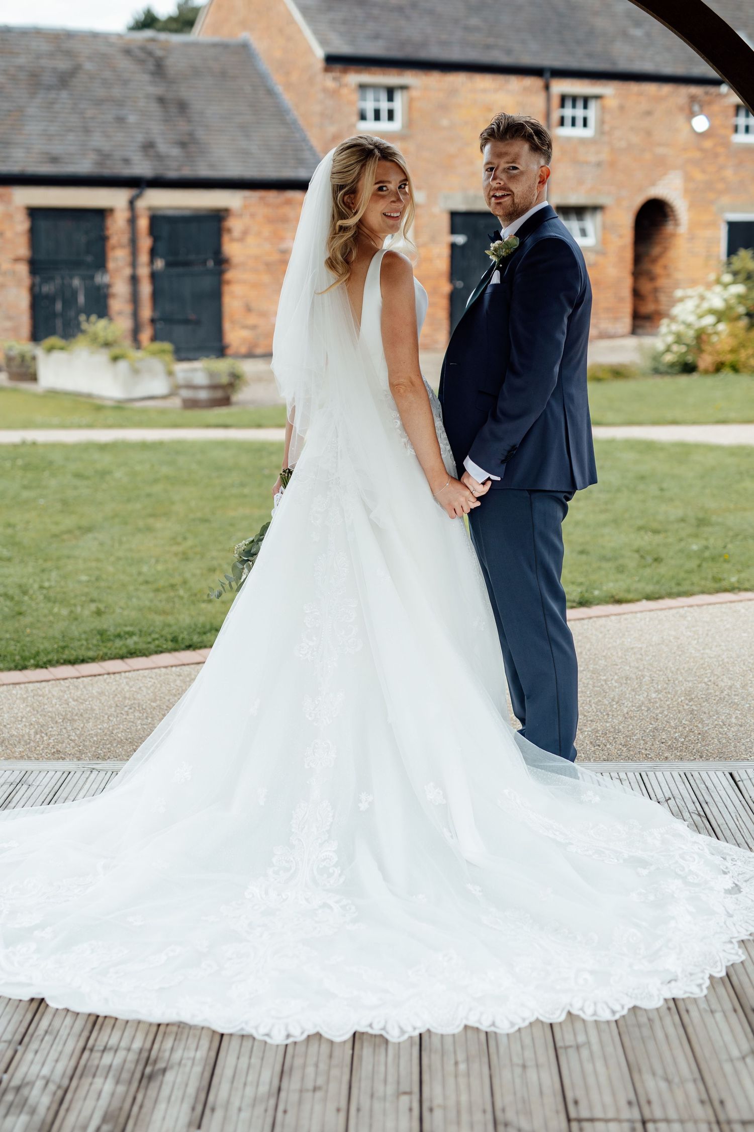 Wedding couple posing on wooden deck with historic brick buildings in background.